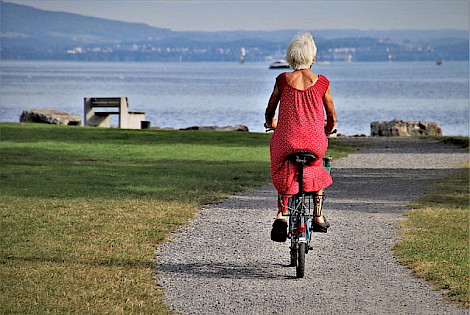 Frau mir rotem Kleid und weißen Haaren auf Fahrrad fährt in Richtung Seeufer